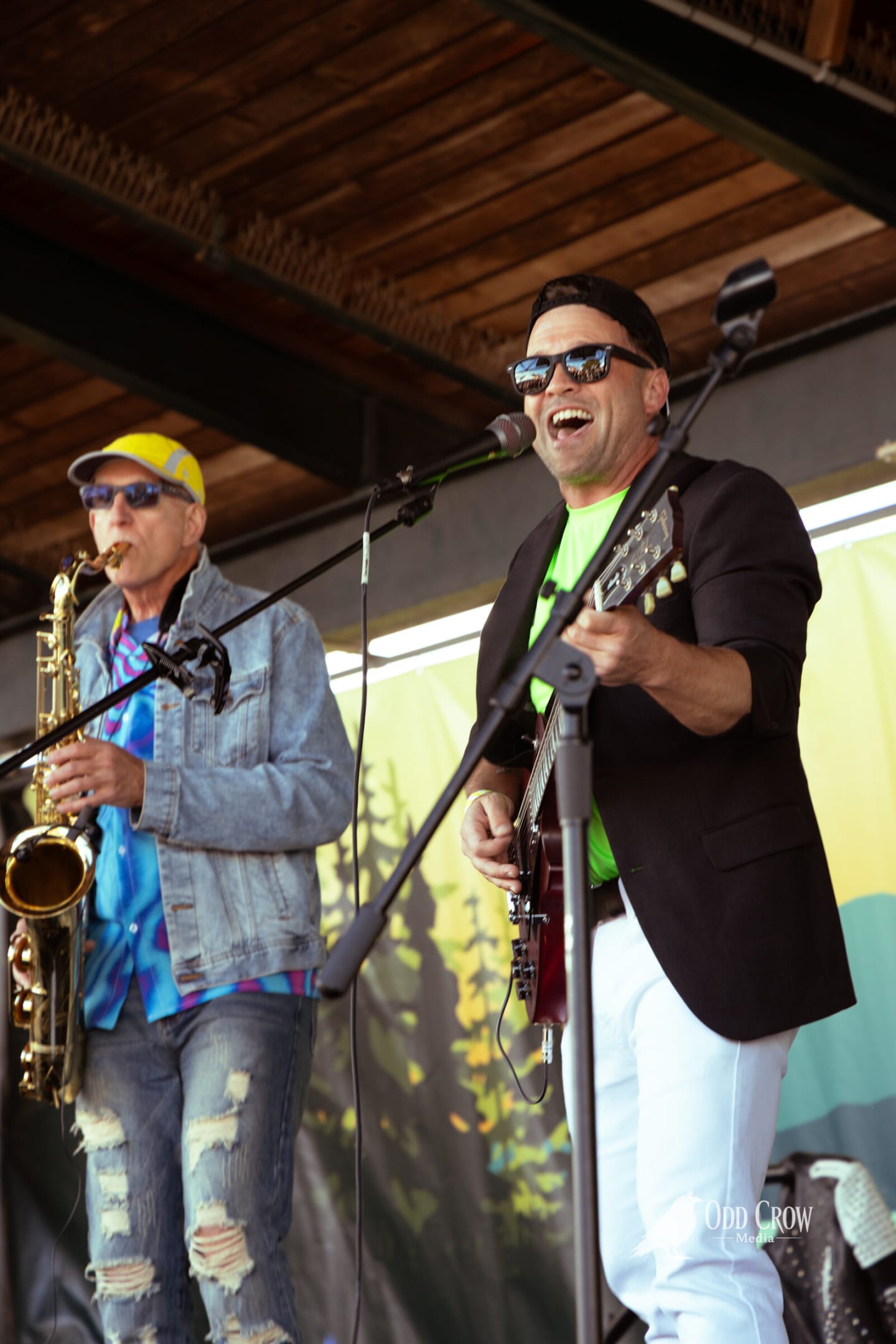 Saxophone player and guitarist in a neon green shirt laughing together on stage