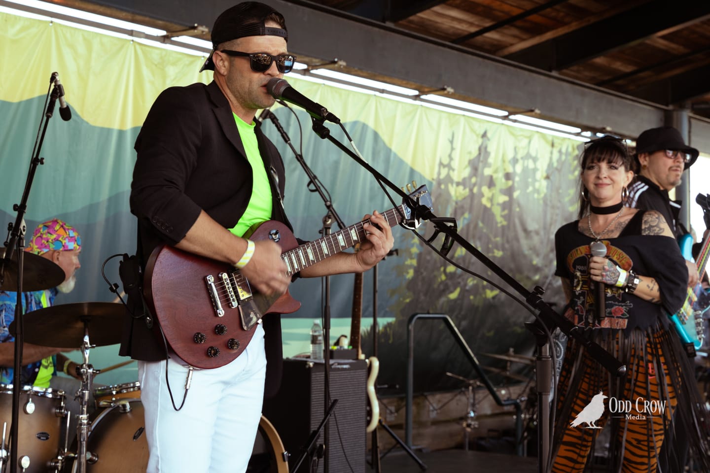 Guitarist in a neon green shirt and black blazer singing and playing, vocalist behind him