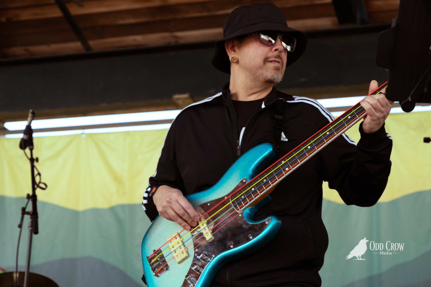 Bass player in a black bucket hat and track jacket playing a teal bass