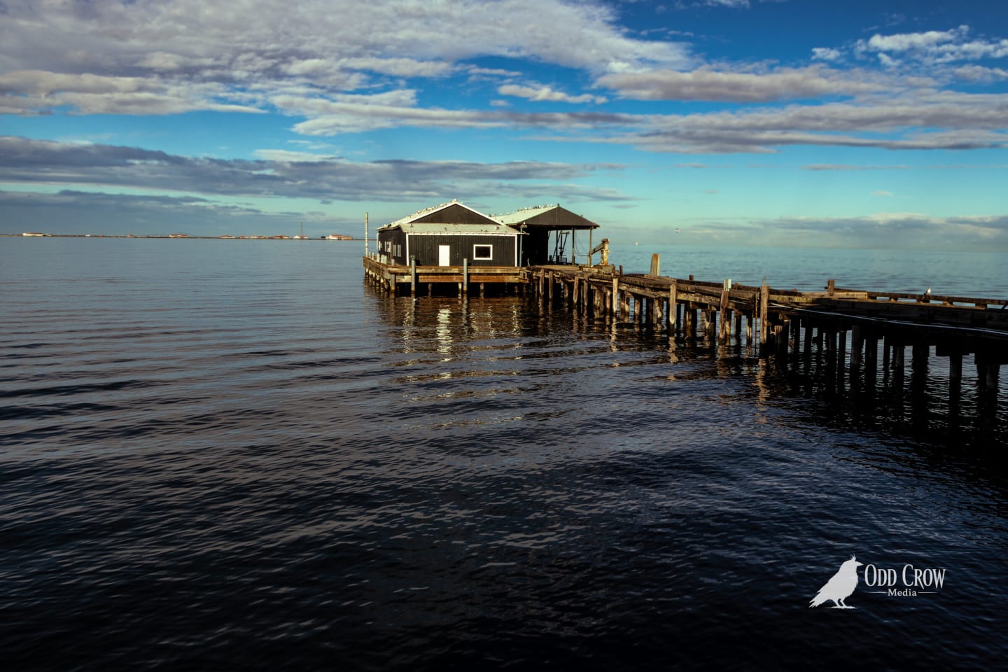 The end of the pier and its small buildings over calm water under scattered clouds