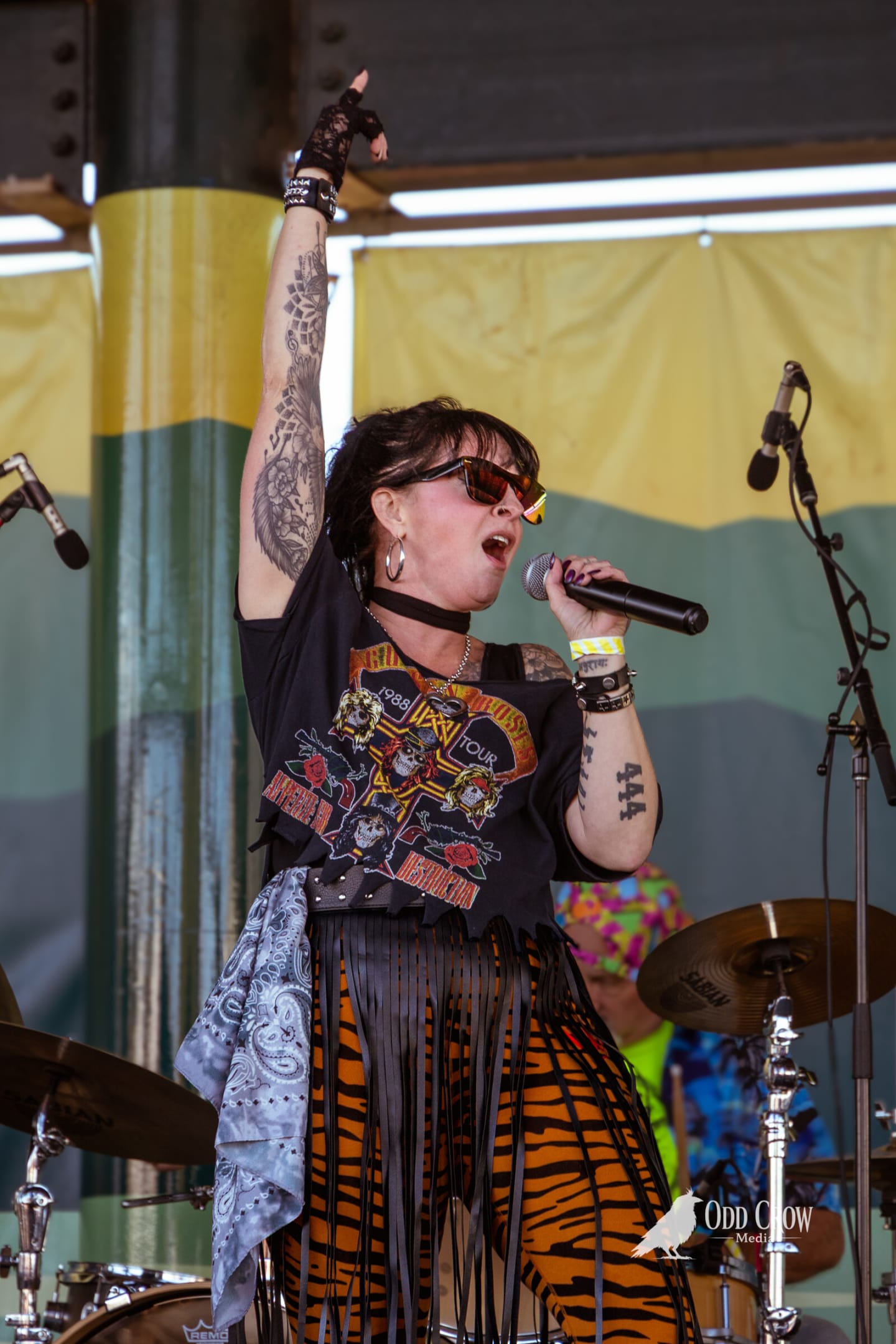 Female vocalist in a Guns N Roses tour shirt and tiger-print skirt singing with her arm raised