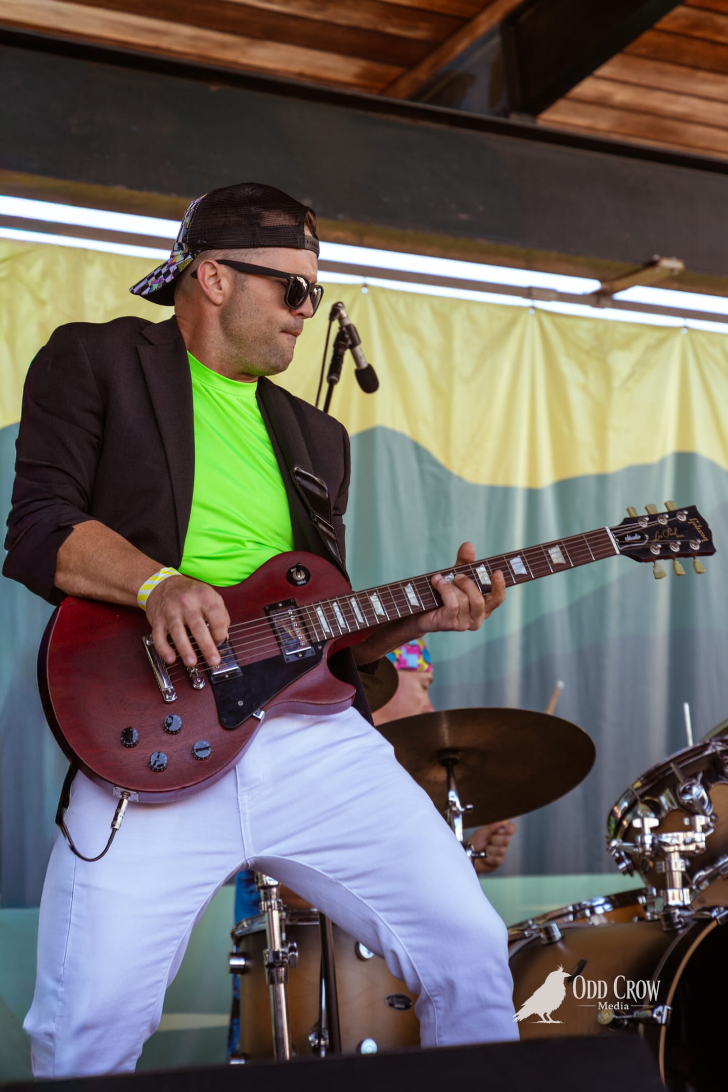Guitarist in a black blazer and neon green shirt leaning into a solo on a dark red Les Paul