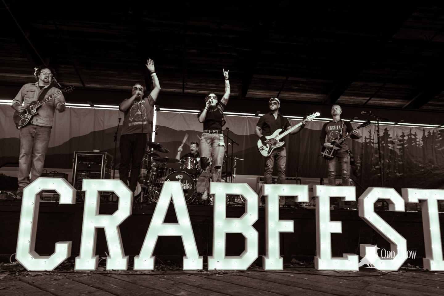 Supernostalgic on stage behind the CRABFEST marquee letters, two vocalists with arms raised, black and white edit