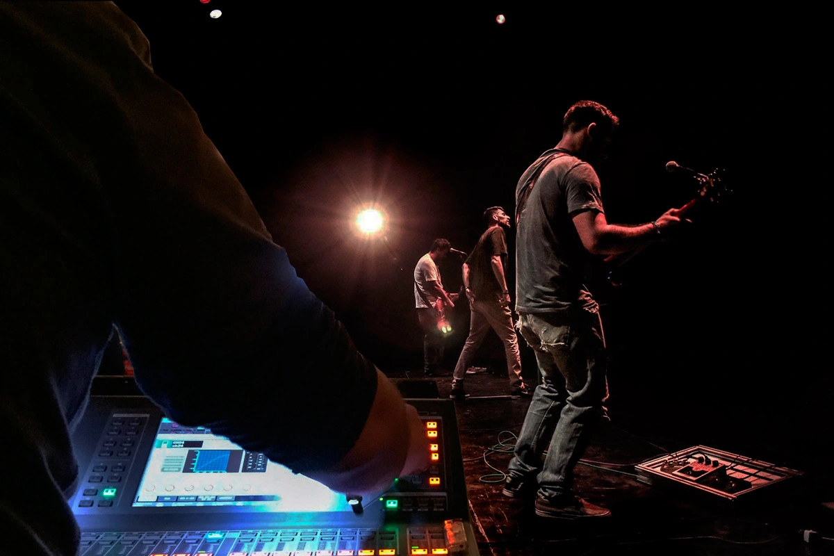 Técnico de monitores al lado de los artístas encima del escenario con la mesa de monitores.