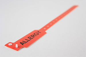 Red patient wristband for hospital admission with sizing holes, snap closure, and "ALLERGY" in large black text.