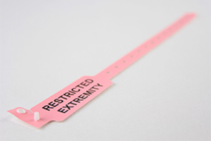 Light pink hospital patient wristband with sizing holes, snap closure, and "RESTRICTED EXTREMITY" in large black text.