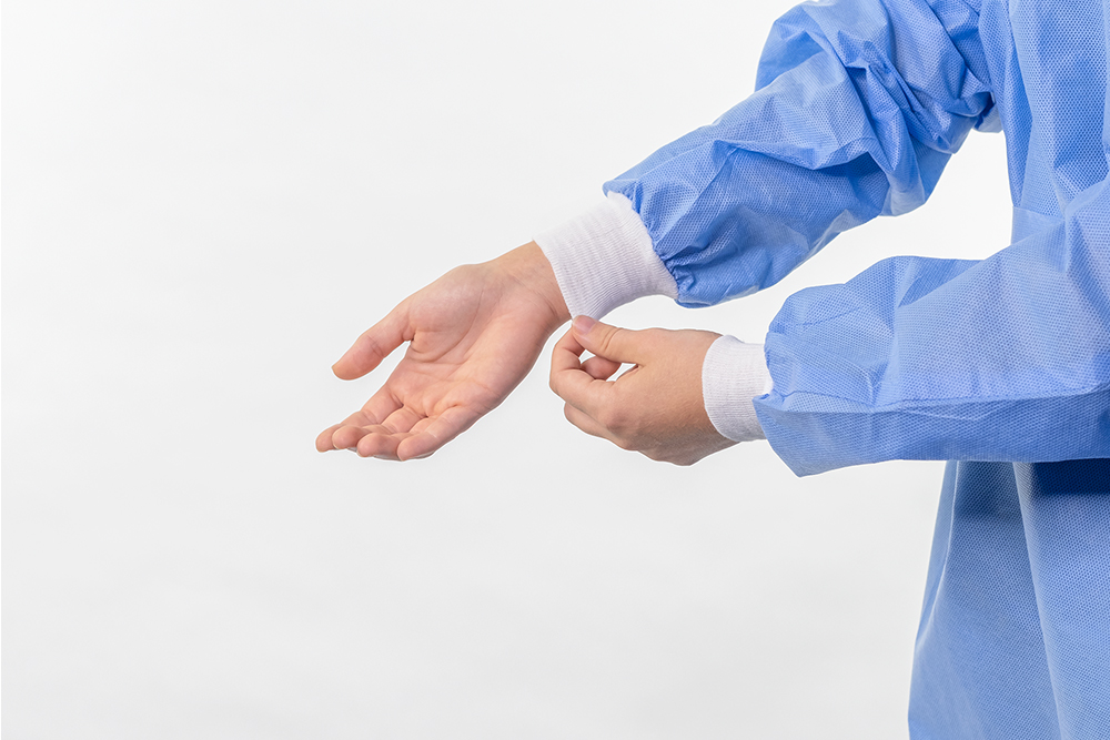 Typenex Medical PPE. Arms in blue disposable medical isolation gown, with white elastic cuffs around wrists.