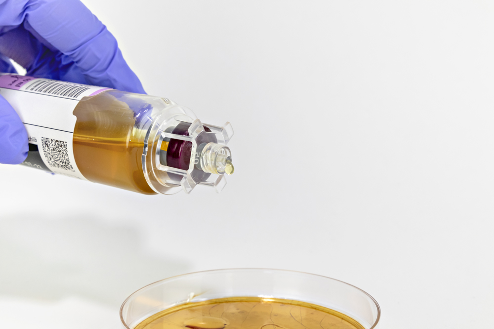 CultureSafe culture bottle dispensing device affixed to a culture bottle dispensing a drop of specimen sample onto a subculture petri dish.