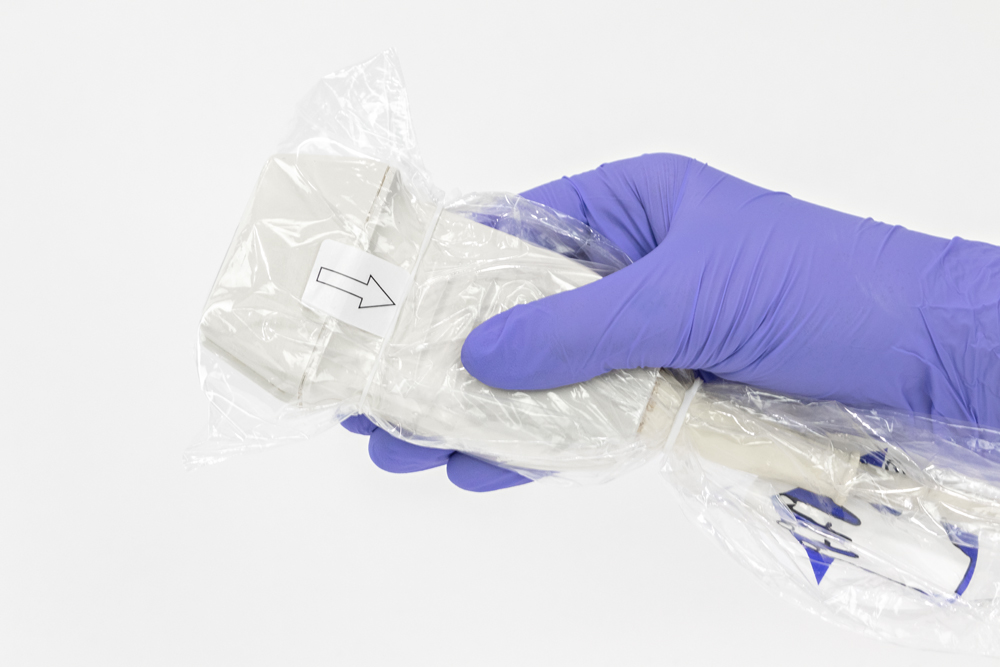 Gloved hand holding an ultrasound probe wrapped in a clear ultrasound probe cover.