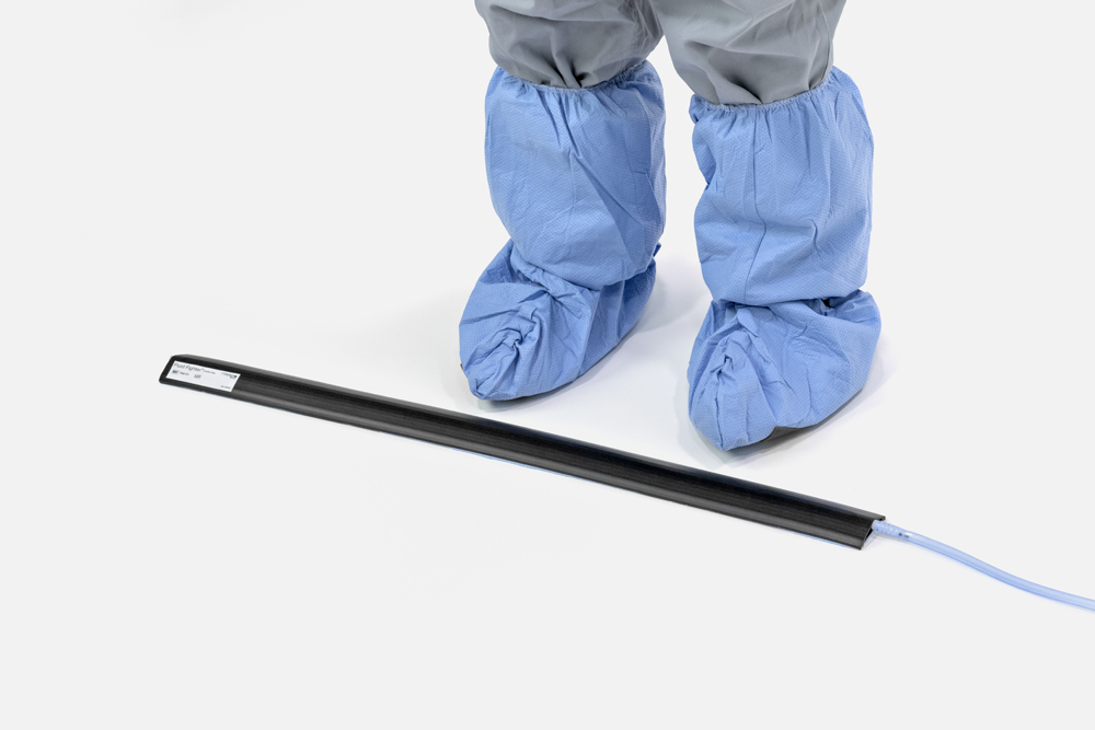 Feet with surgical shoe covers standing next to a Fluid Fighter Suction Strip floor fluid waste barrier. (FM0701)