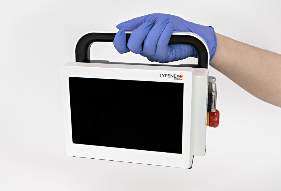 A gloved hand lifting up a Fibernex Go Laser Generator by the unit’s handle.