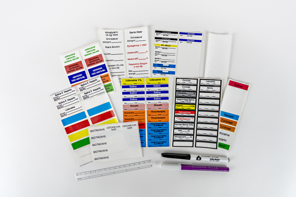 Assortment of custom sterile medical labels in various colors showing pharmaceutical options including Lidocaine, Saline, Sheath, Epinephrine, Thrombolytics, Heparin, and Contrast agents, with blank templates and markers.