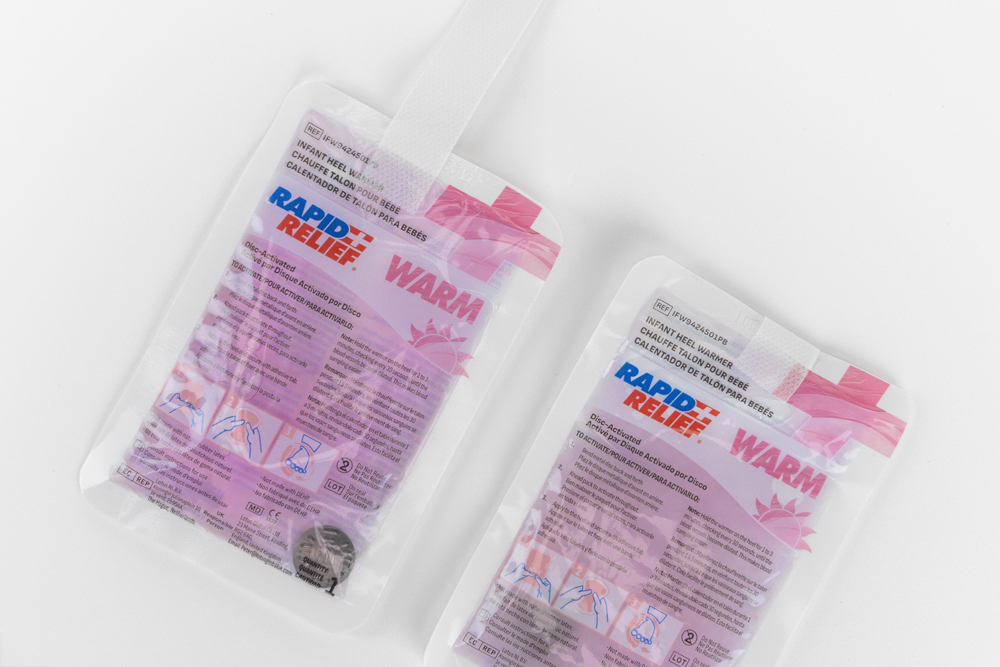 Two infant heel warmer packages shown at an angle, displaying product information and heat activation instructions.
