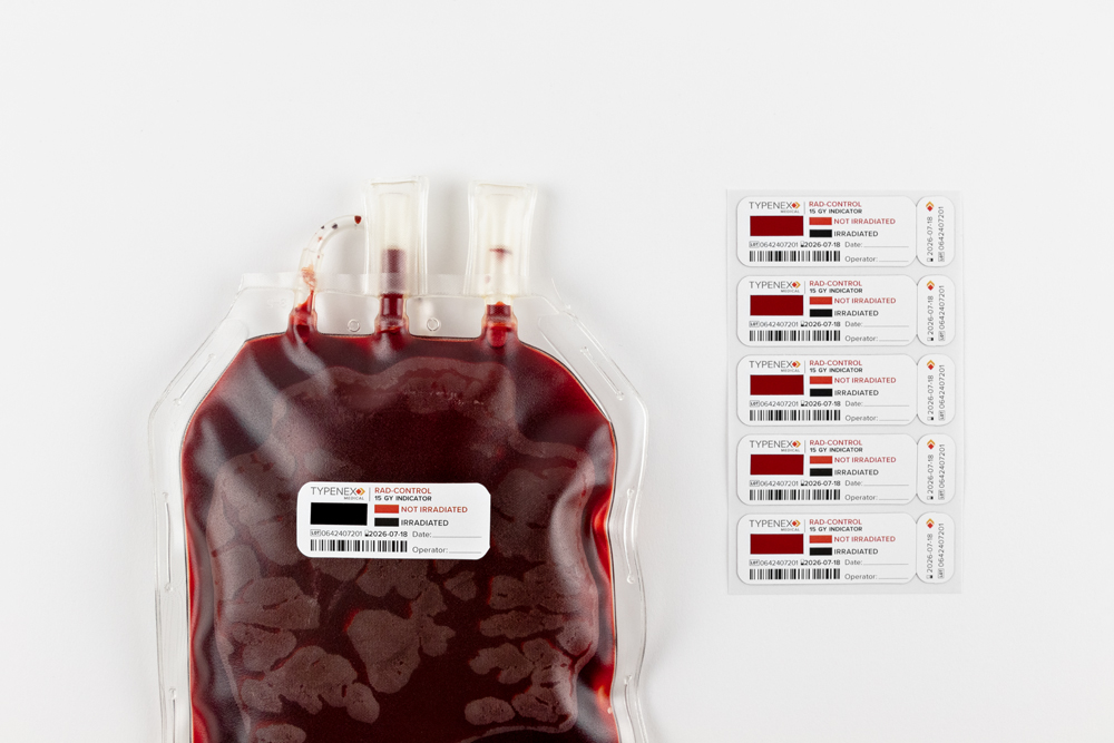 Blood bag with an irradiated Rad-Control 15 Gy indicator, beside a sheet of unused irradiation tags.
