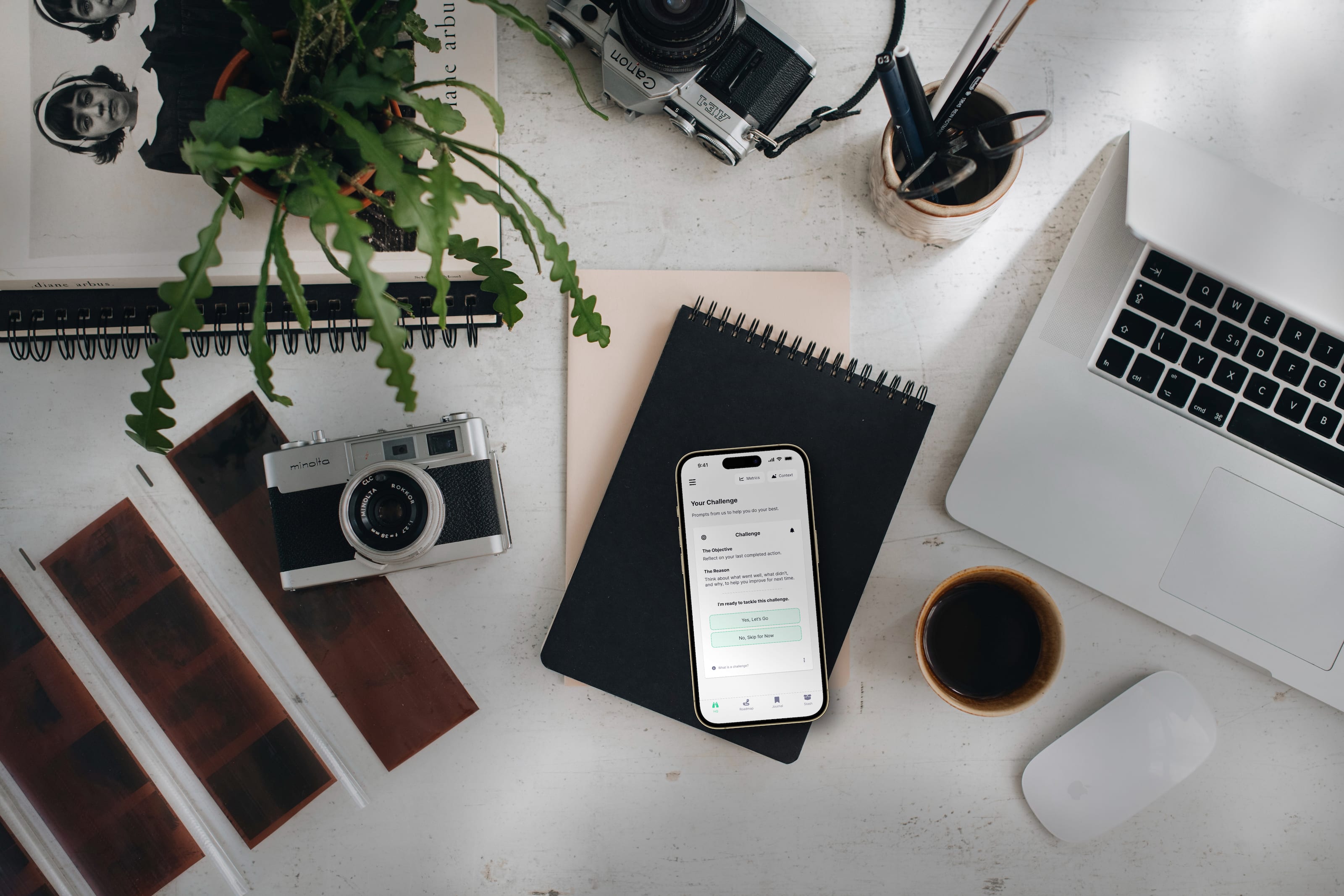 Top down view of an iPhone 14 Pro with the YearWeGo app on a table with an Apple Laptop, cameras, and other items.