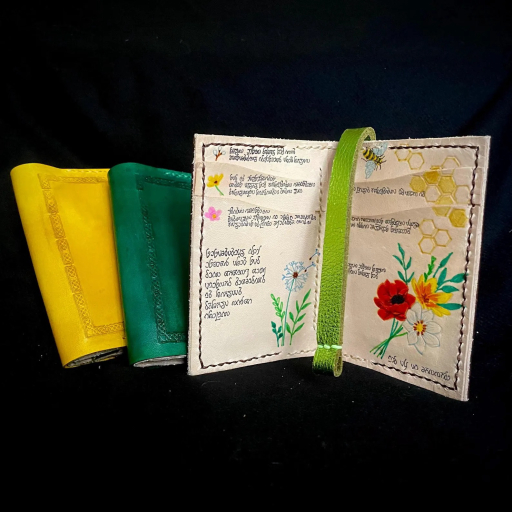 An image showing three bifold wallets against a black background. Two wallets are closed to showcase the celtic knotwork tooling on the exterior, while the third is open to show that the interior looks like the inside of a spellbook that details the magical use of plants. 