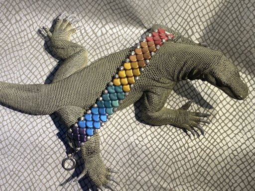Bob the Komodo dragon toy modeling a Czech glass dragon scale rainbow pride bracelet on a silver scaly background 