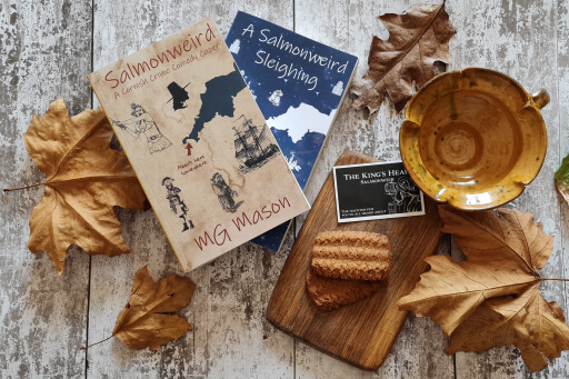 Flat lay of books Salmonweird and A Salmonweird Sleighing. Chopping board, medieval pottery and autumnal leaves.