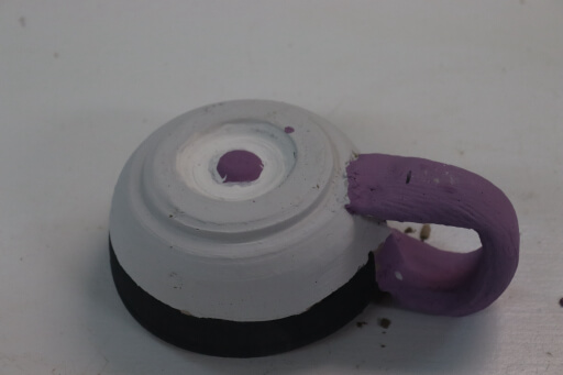 An upside down mug with unfired glaze.  The colors are purple, white, grey, and black