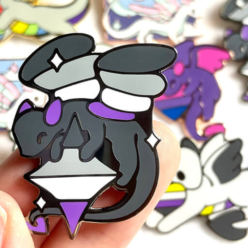 A close-up photo of a small asexual flag enamel pin, shaped like a dragon holding a star. In the background are more dragon pins representing different flags.
