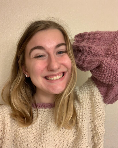 Sammy is a white woman with blonde hair. She is wearing a handknit pink and white sweater.