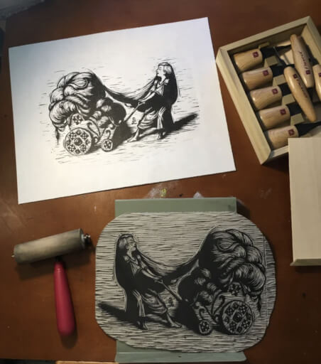 A photo of a linocut print depicting Rapunzel pulling her hair in a wagon, showin next to the linocut block and printing equipment used to make it.
