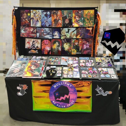 Artist Alley table of prints, stickers, and acrylic charms (of fanwork and original artwork) by NULLIPHY (Paige Grigg)