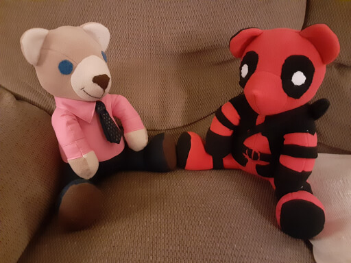 Two handmade teddy bears sit in an easy chair. The bear on the left is light brown and dressed like a lawyer, complete with pink button-down shirt and navy blue trousers and tie. The bear on the right is red and black and resembles the Marvel character Deadpool.