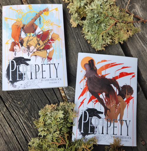 Two comic books titled Peripety volume one and two on a dark wooden backdrop framed with cedar branches.