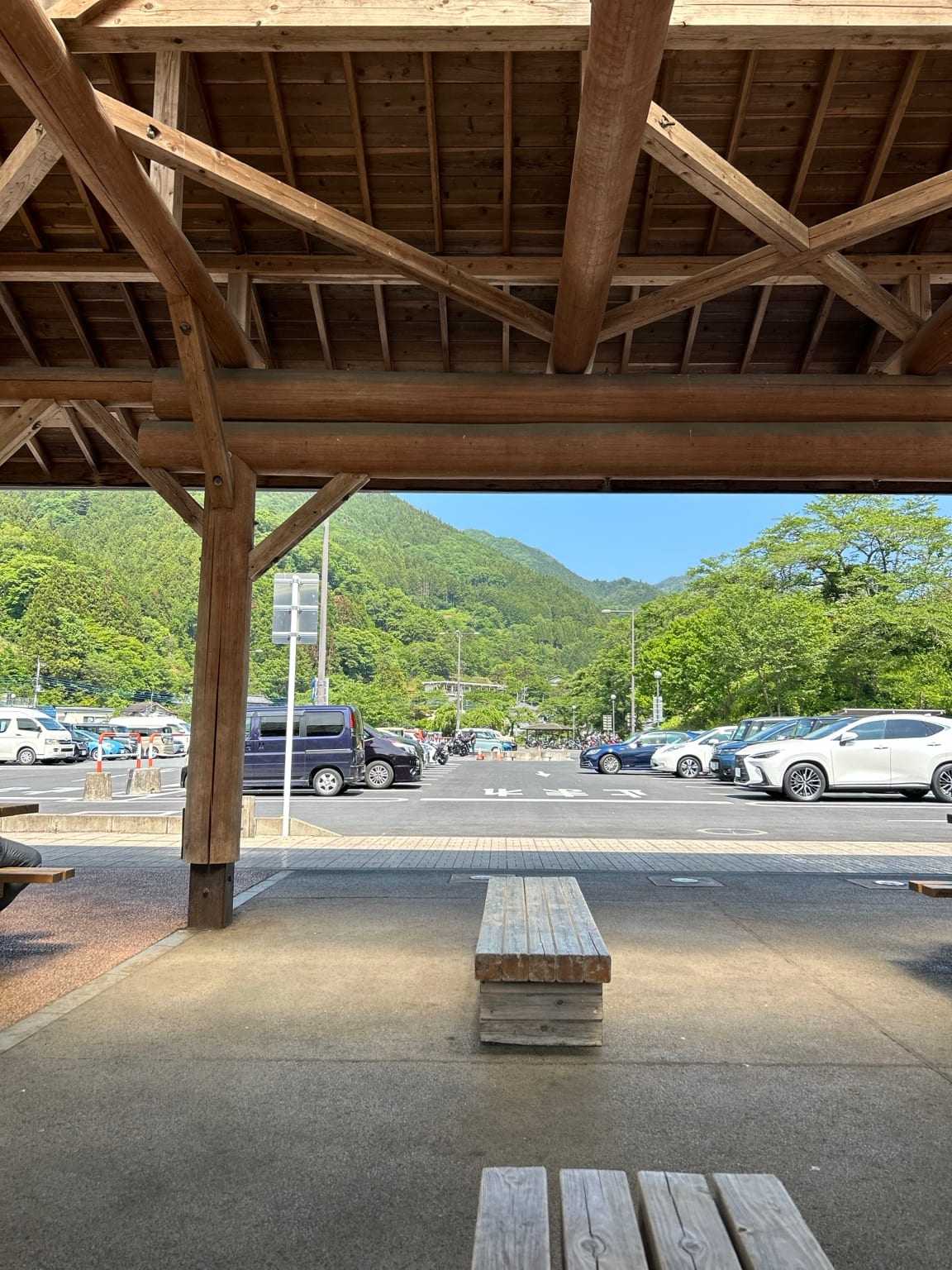 大きな木造屋根とベンチ越しに見える駐車場と山並み