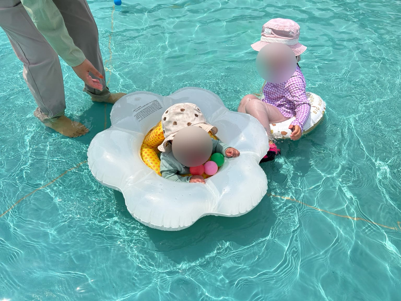 白い花形の浮き輪に座る0歳児と隣で見守るきょうだい