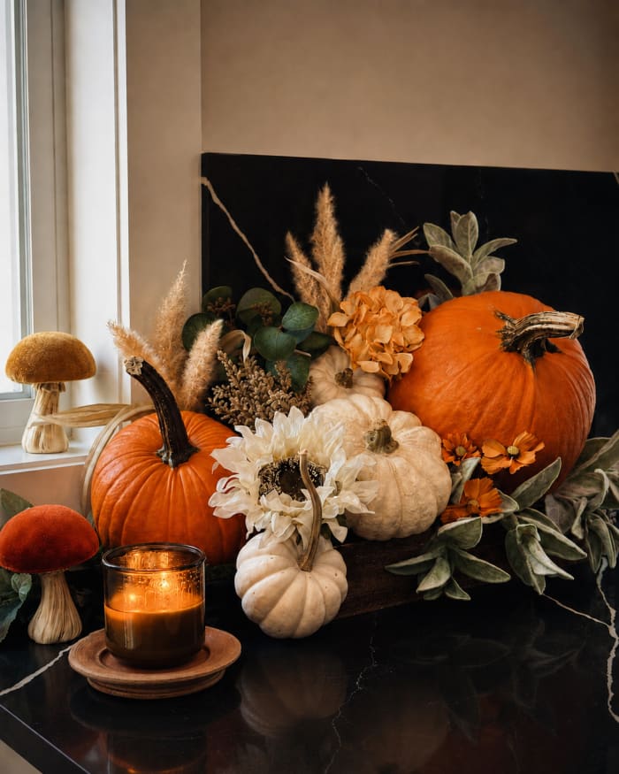 Pumpkins and gourds in cream, clay, and deep orange are softened by flowers, feathery grasses, velvety leaves, and a single pool of candlelight.