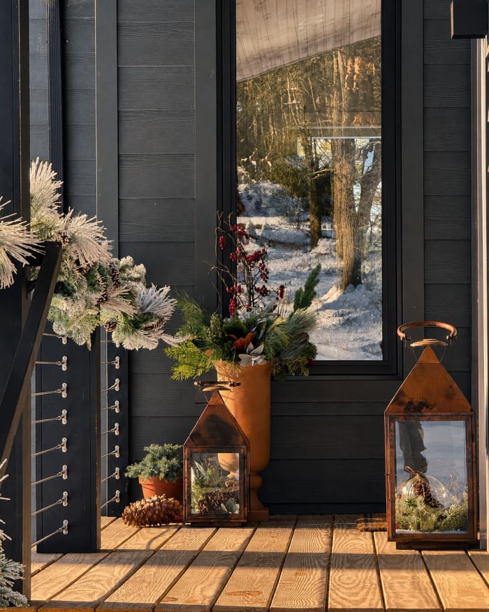 Evergreen, winter branches, and burnished lanterns make the first gesture, set against the stillness of the snow.