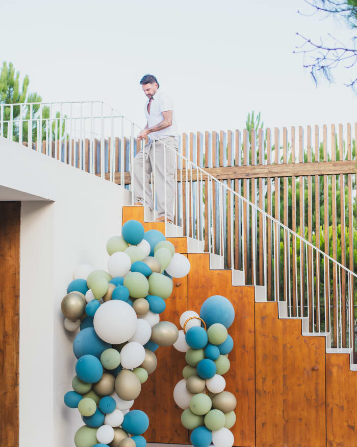 Oversized balloon installation in sea blue, sage, ivory and muted gold beneath an outdoor staircase in Comporta, Portugal.