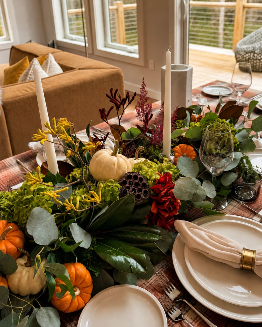 An autumn table run with magnolia, eucalyptus, hydrangea, seed pods, and small gourds on warm plaid.