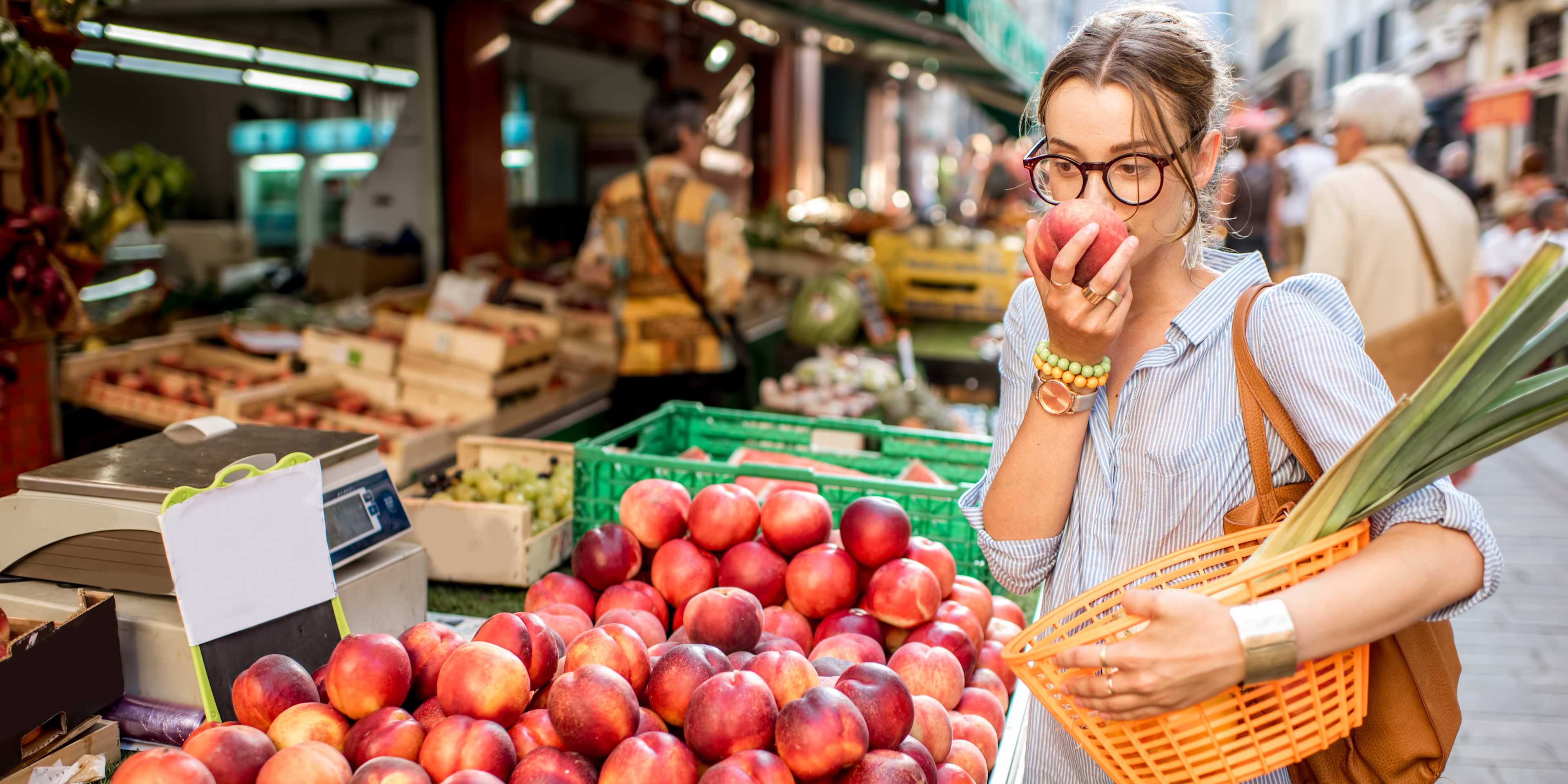 woman at a food market smelling fruit for some reason