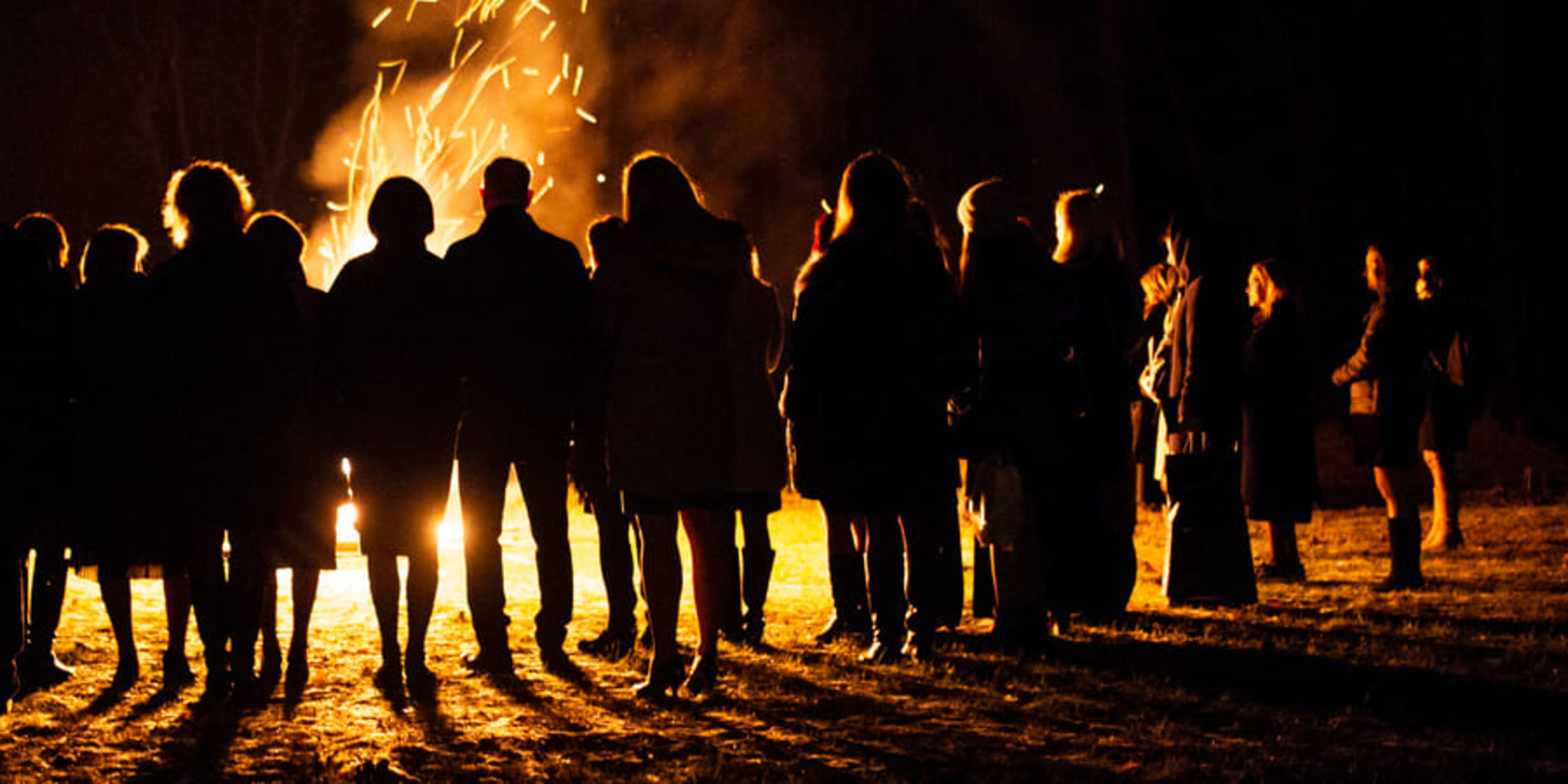 Group of people silhouetted against a beach bonfire at night