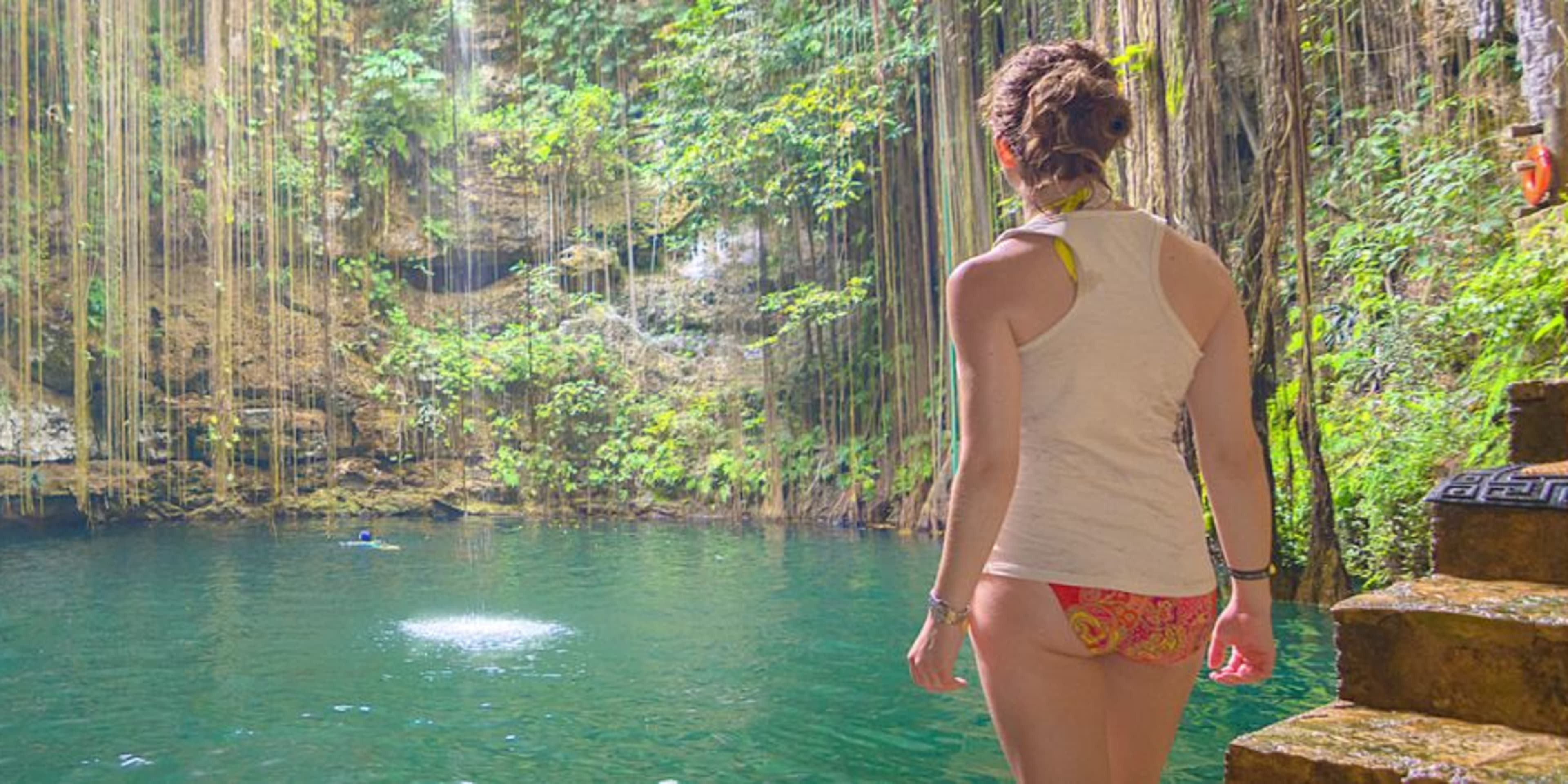 Back view of woman in swimwear overlooking blue swimming lagoon with tropical vegetation