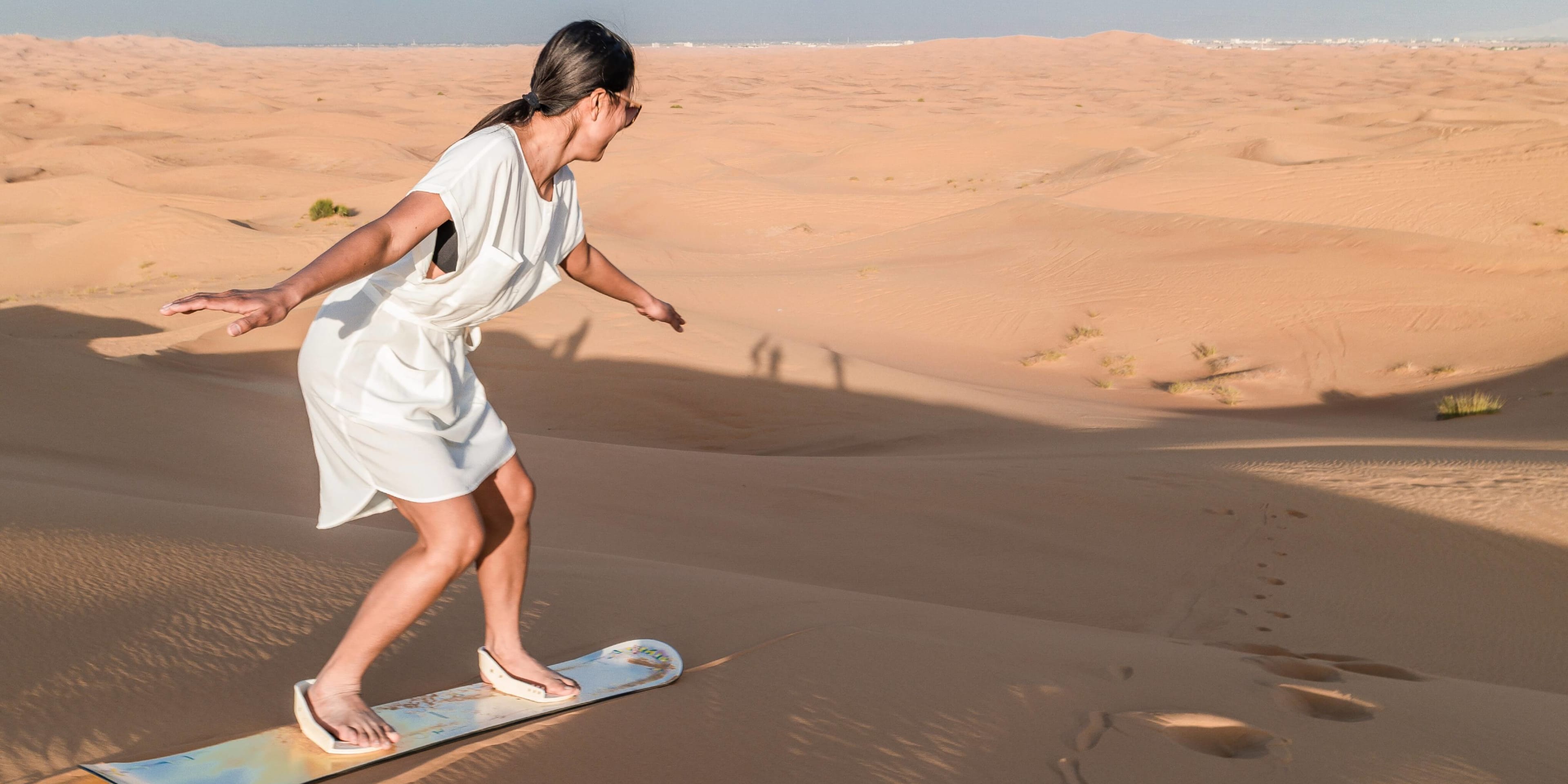 A woman tries sandboarding down a Dubai desert dune