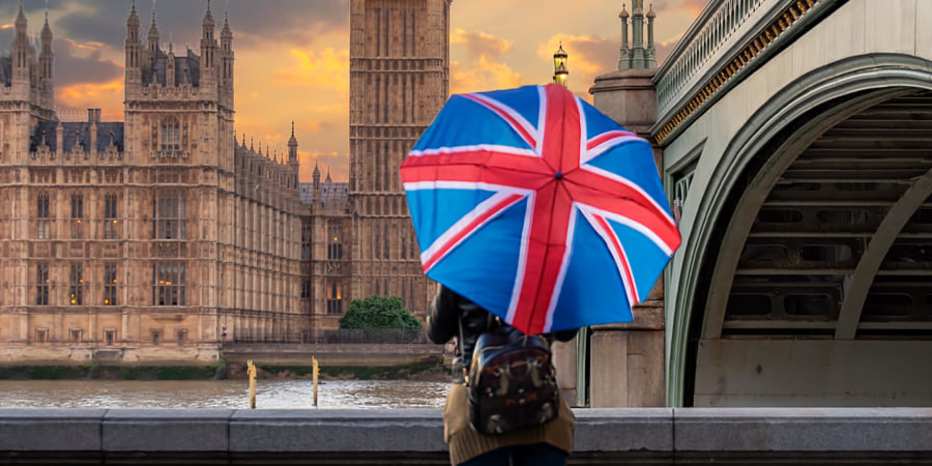 Turista com guarda-chuva da bandeira do Reino Unido olhando para o Big Ben do outro lado do Rio Tamisa