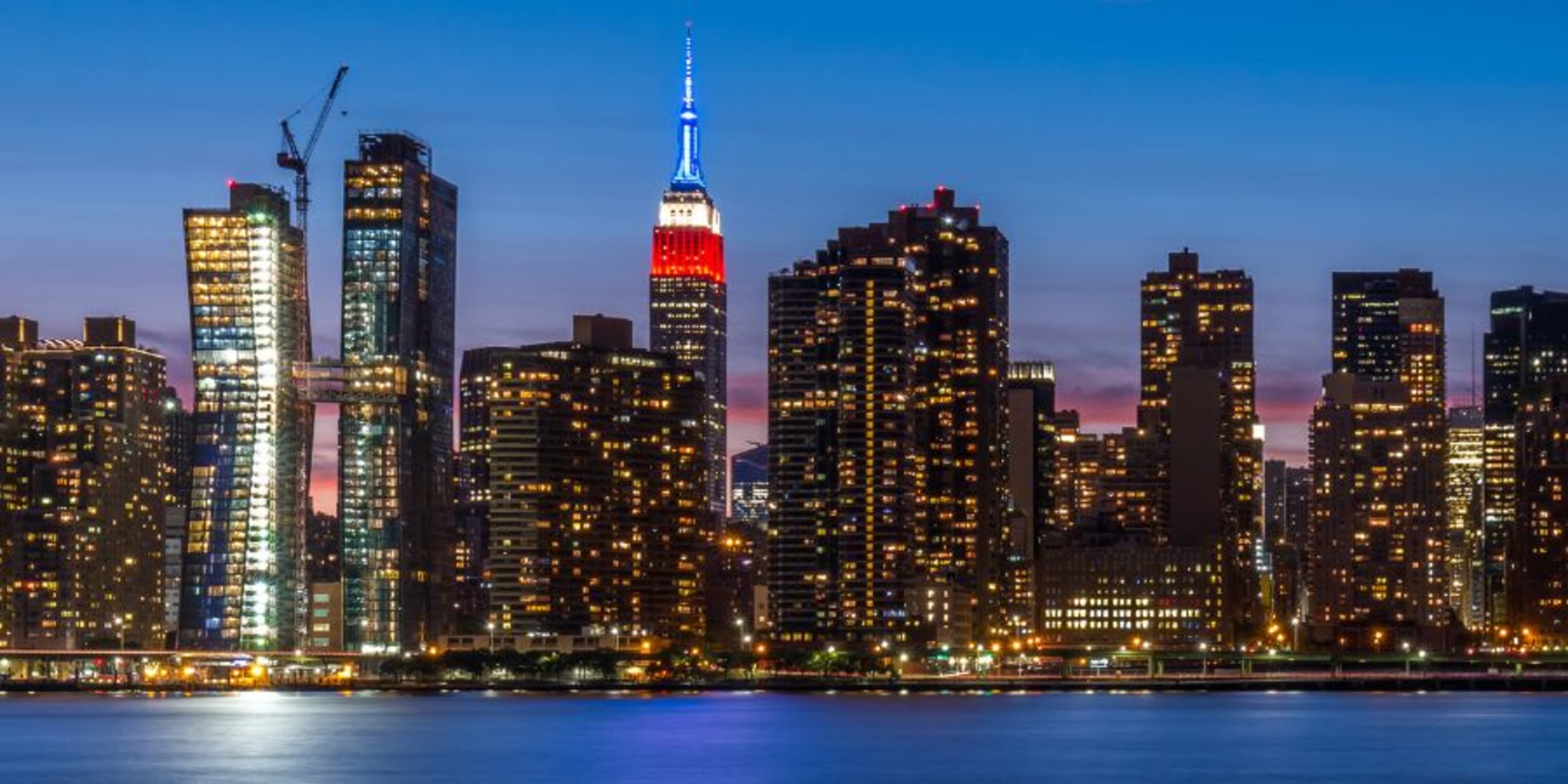 L'horizon de New York de nuit avec les fenêtres éclairées, ainsi que les sommets illuminés de l'Empire State Building et du Chrysler Building.