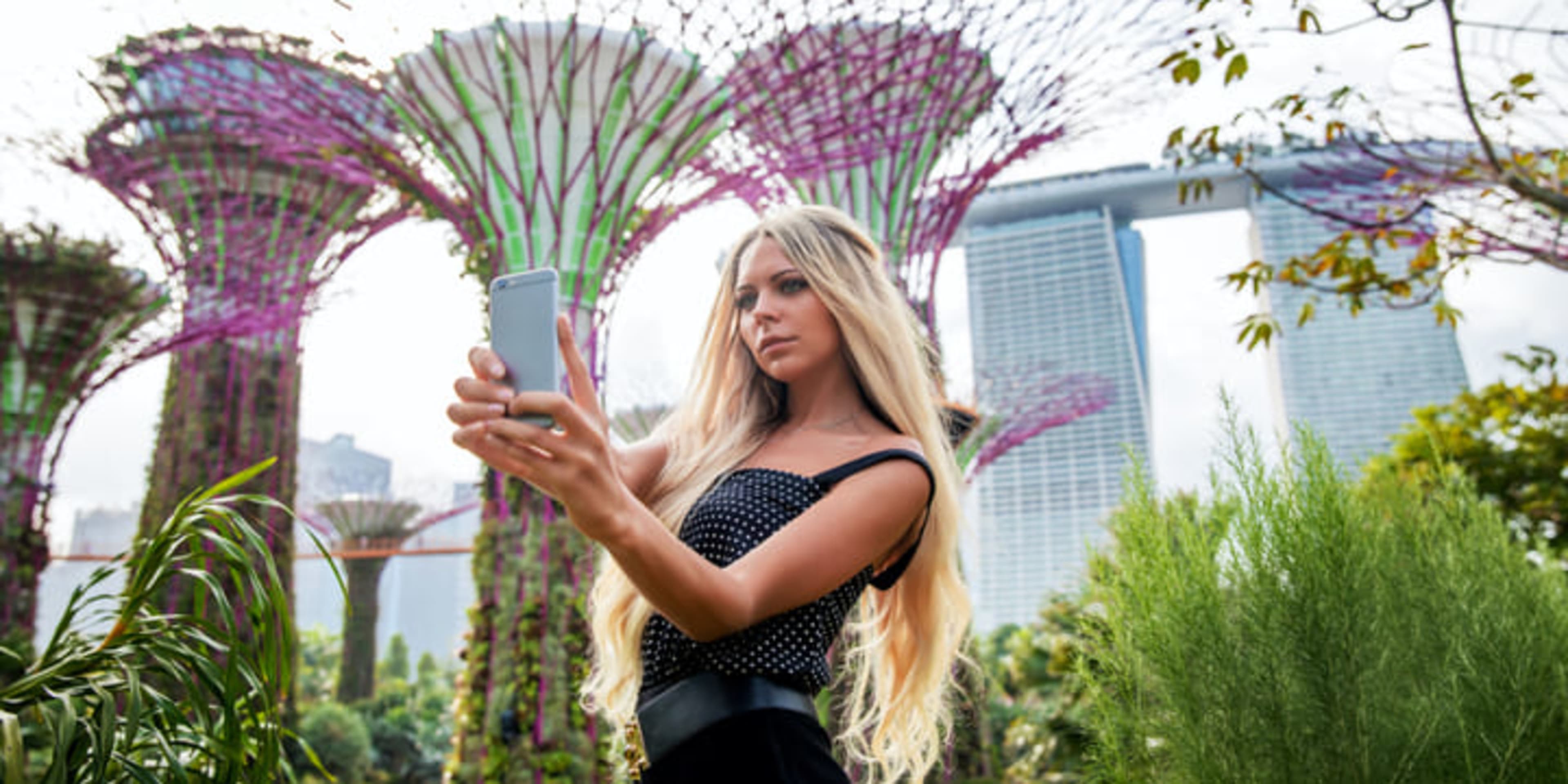 Young woman taking a selfie in front of the supertree structures at the Gardens by the Bay, Singapore