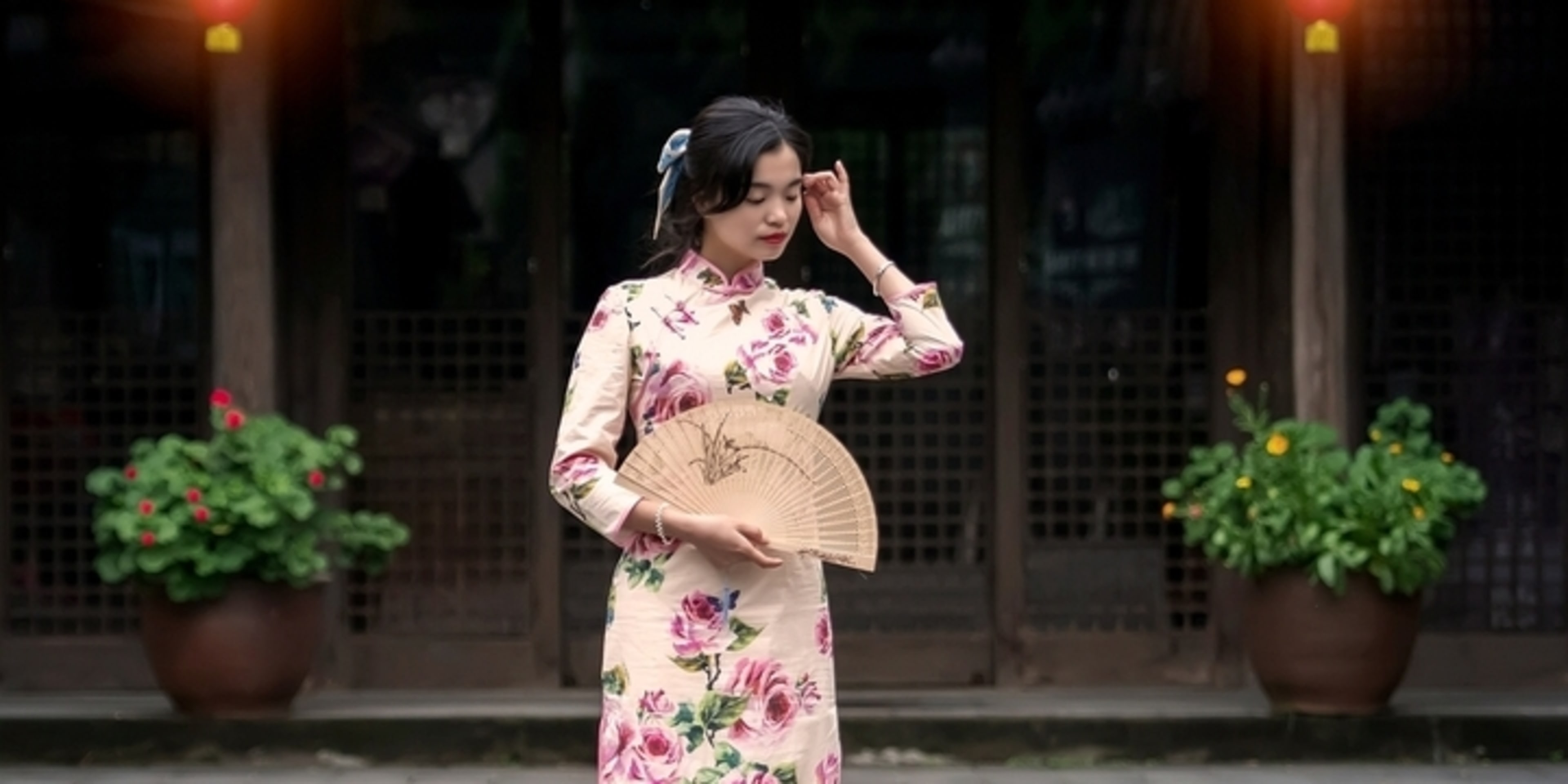 Mujer con un vestido cheongsam tradicional de flores sosteniendo un abanico de papel.