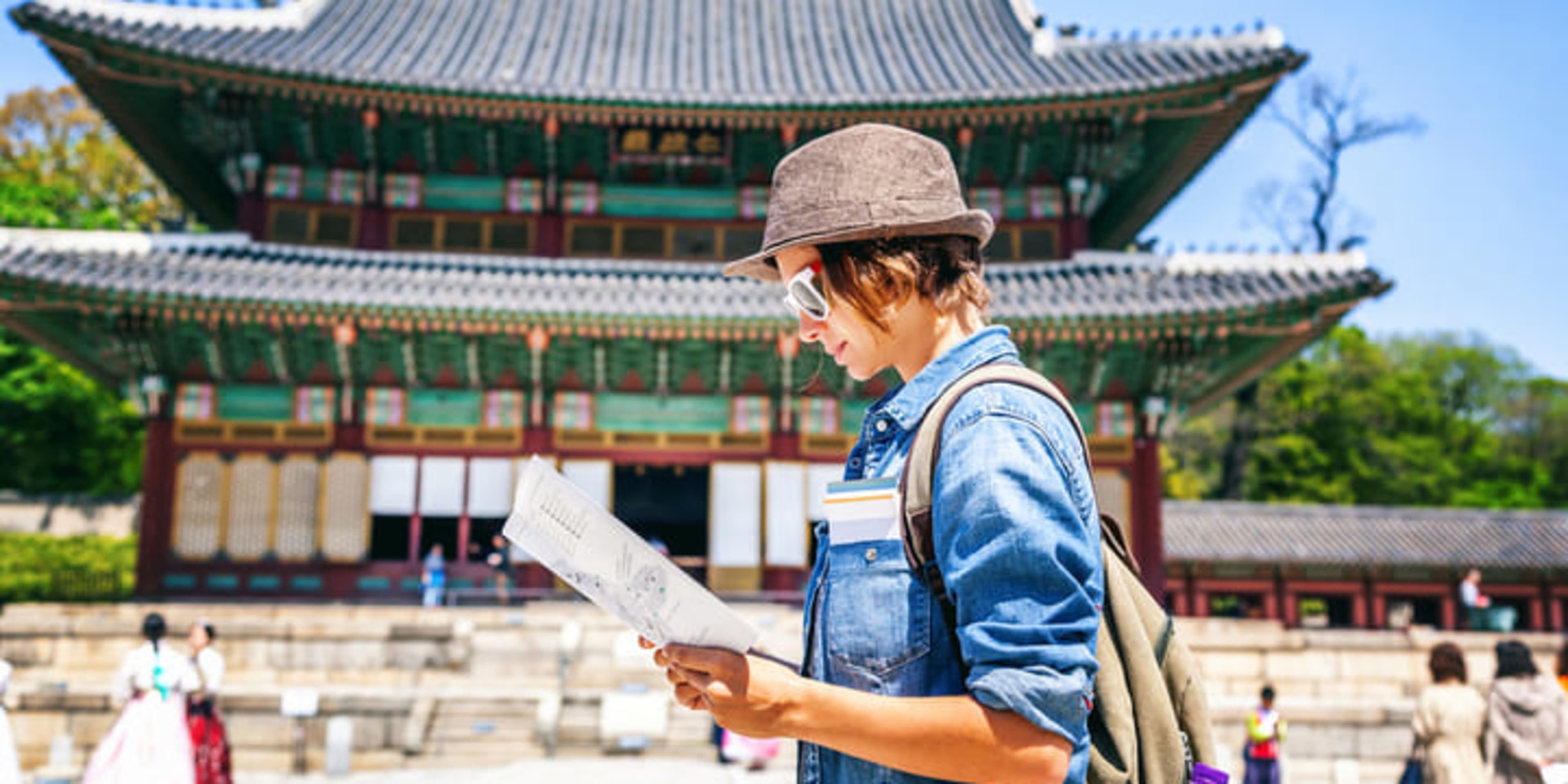 Woman studying a map in front of a pagoda-style building in Seoul.