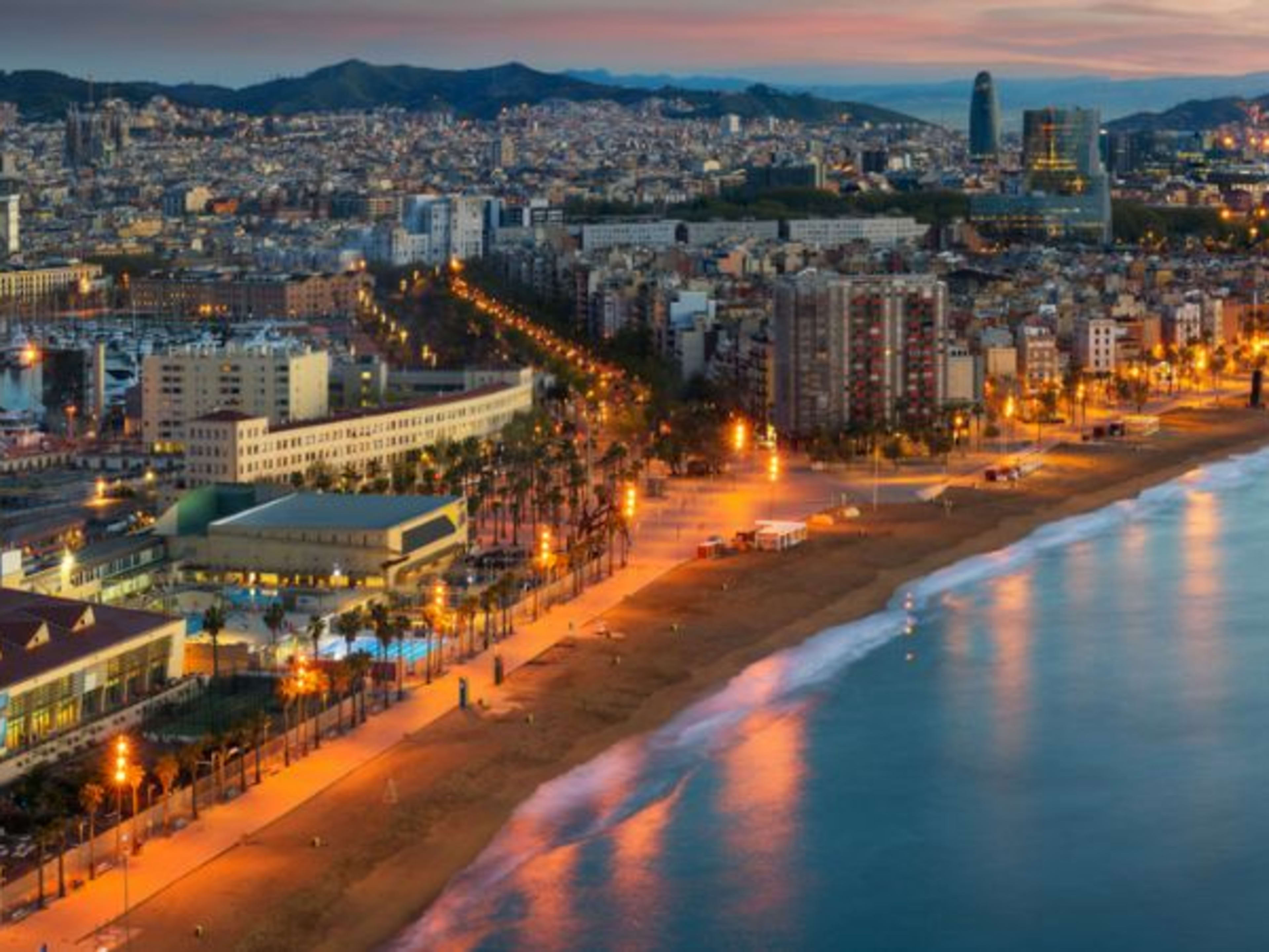 Wide view of Barcelona showing the curve of the bay and the lights of the city as golden evening falls