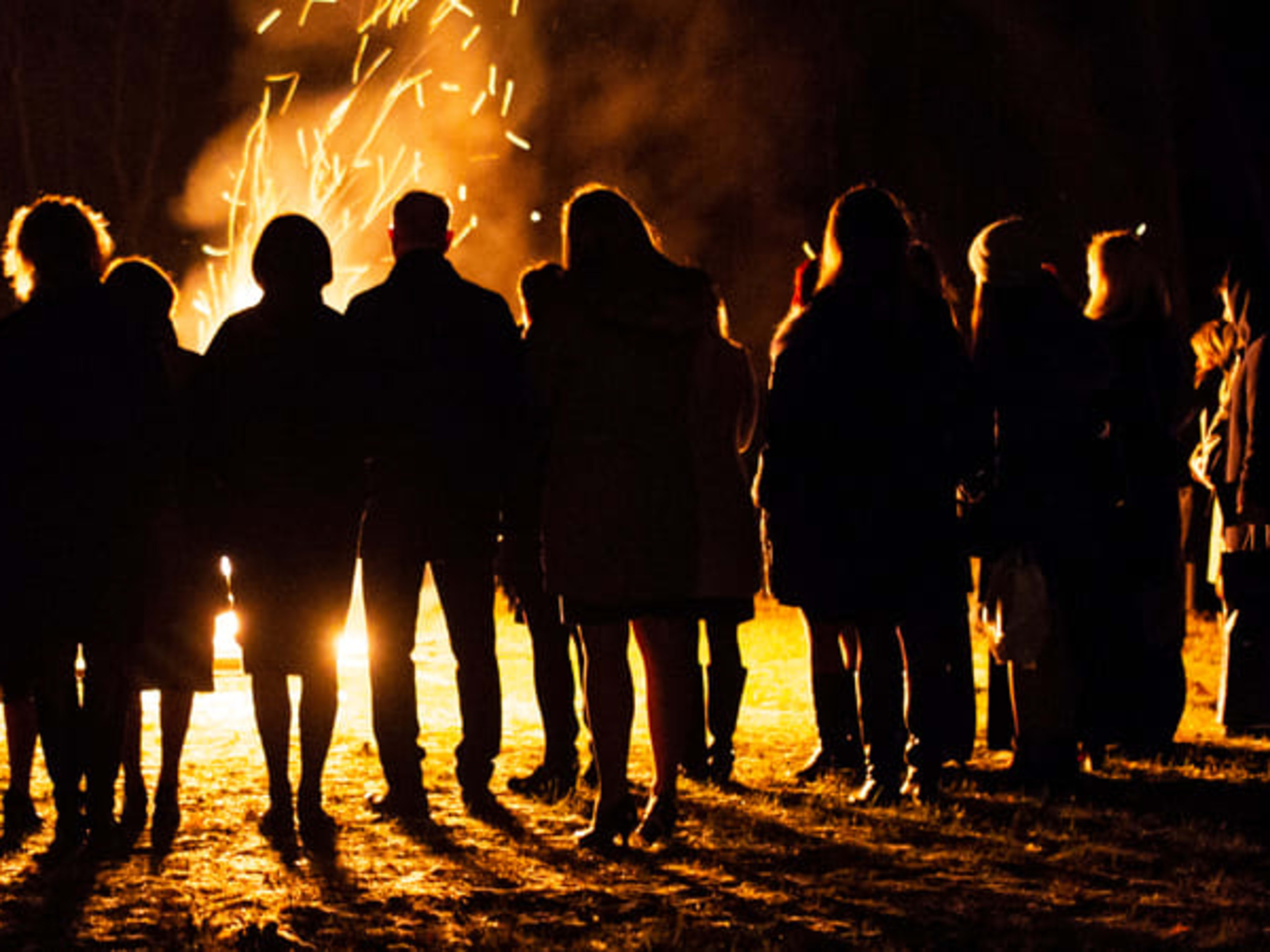 Group of people silhouetted against a beach bonfire at night
