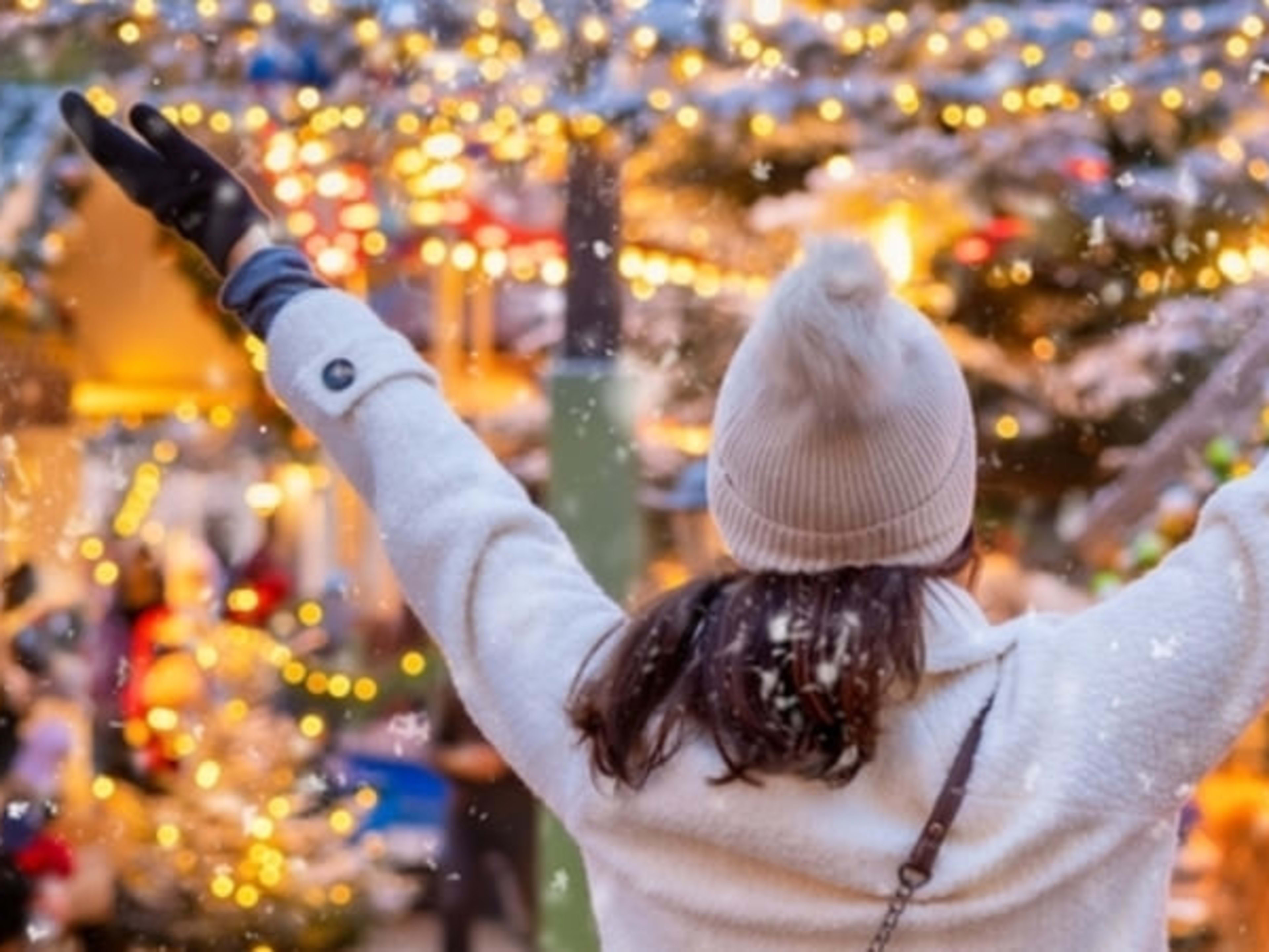 Woman raising her arms in joy at a Christmas market.