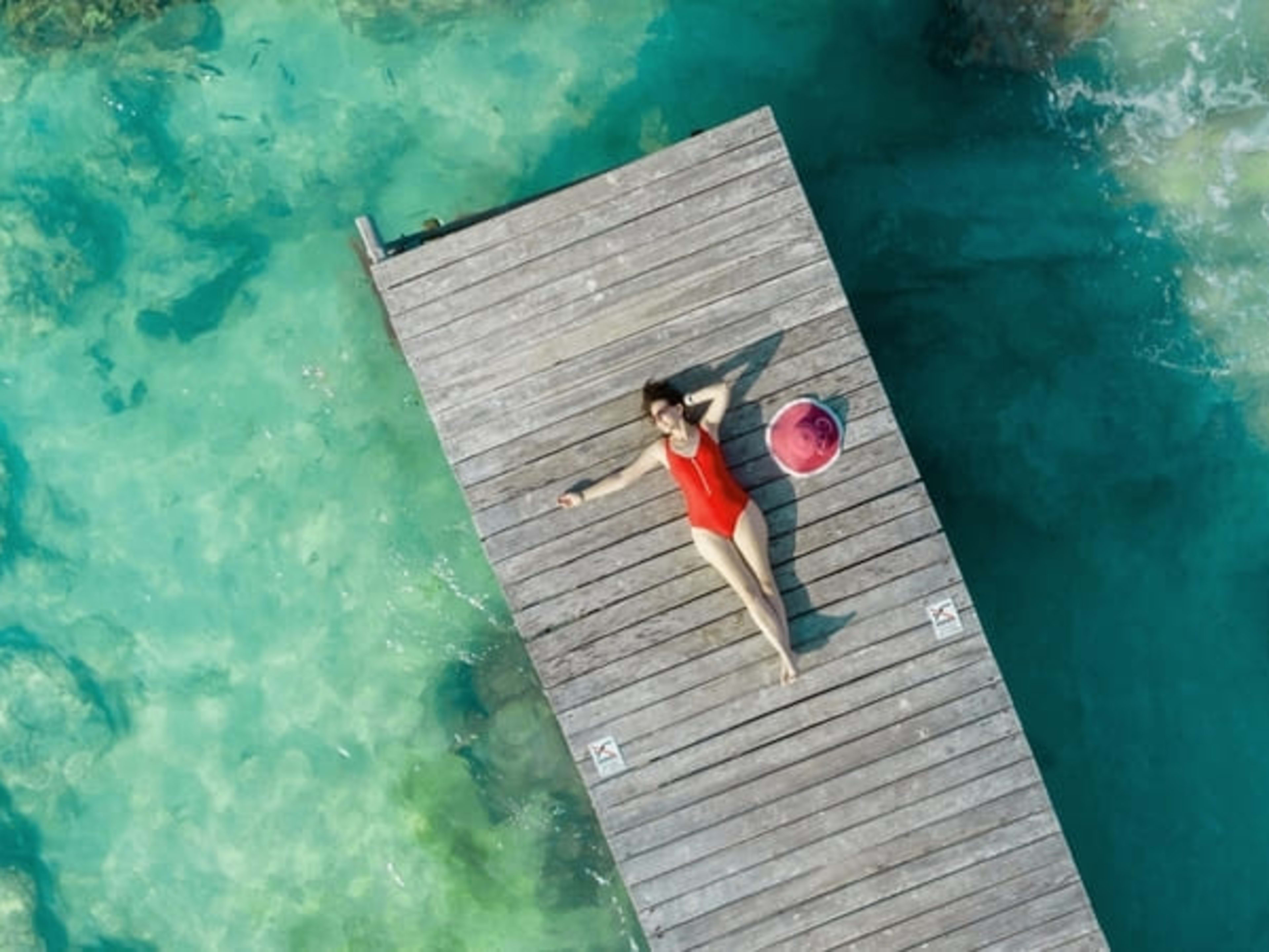 Woman sunbathing on a wooden pier over tropical waters