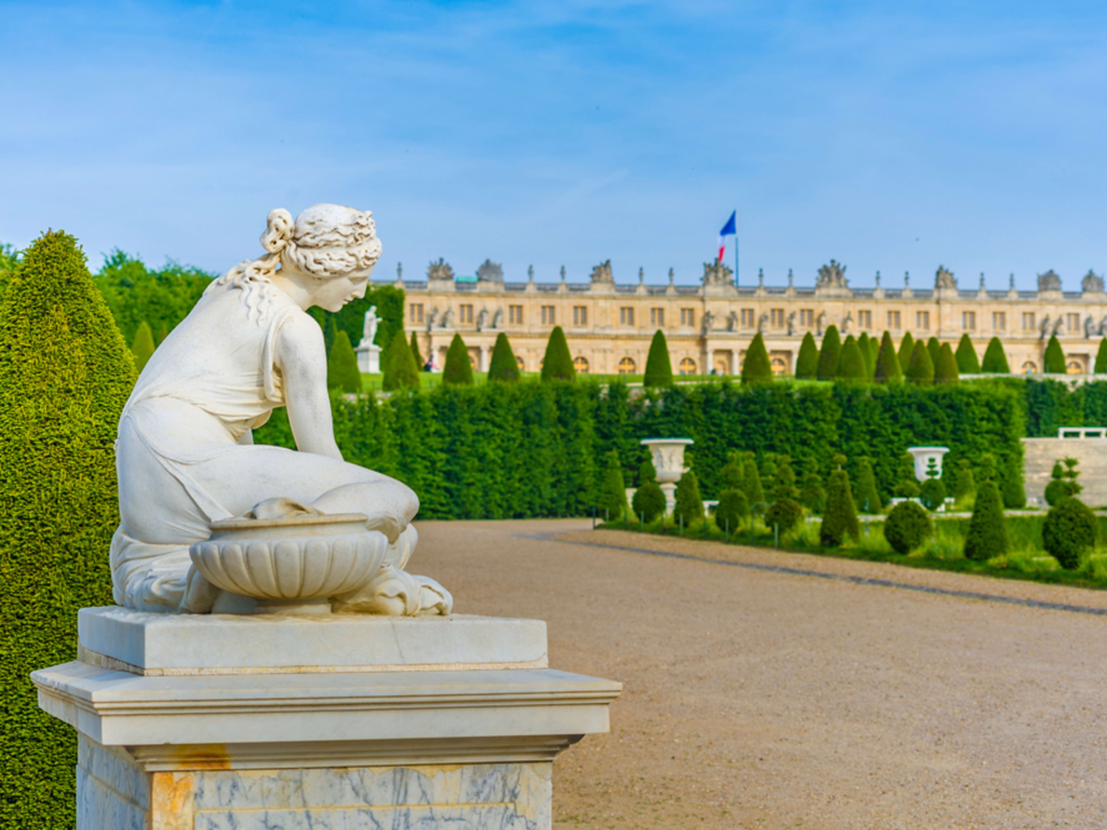 Estatua de los jardines de Versalles con el palacio al fondo. Castillos cerca de París.