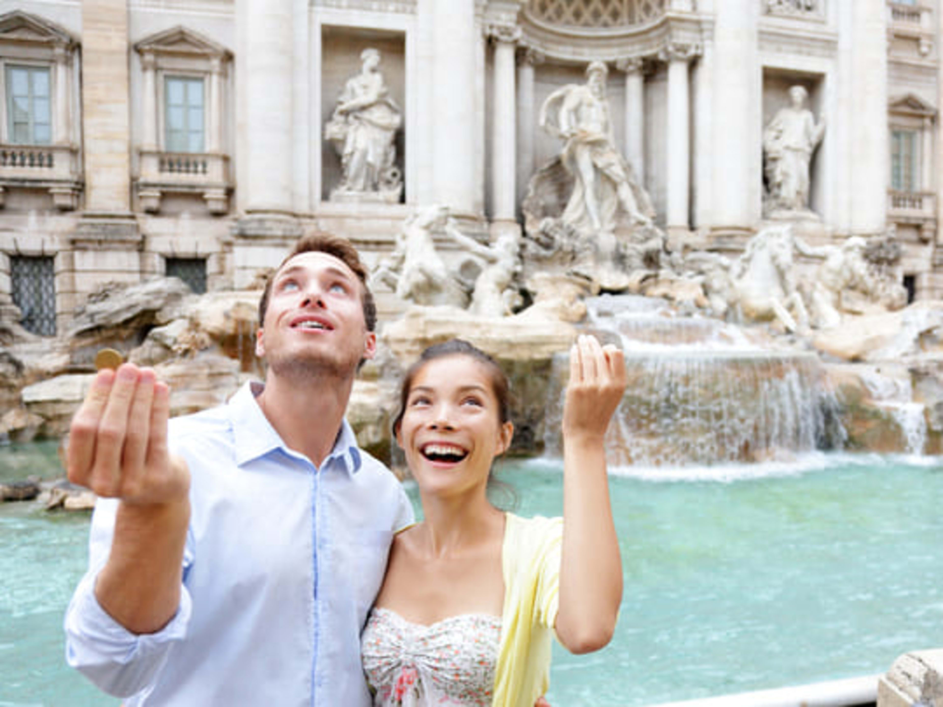 Couple throwing coins over their shoulders into the Trevi Fountain in Rome